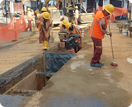 Obreros con cascos y chalecos de seguridad trabajando en una excavación para instalación de tuberías.