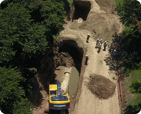 Excavación en una vía con maquinaria pesada y trabajadores realizando labores de instalación subterránea.