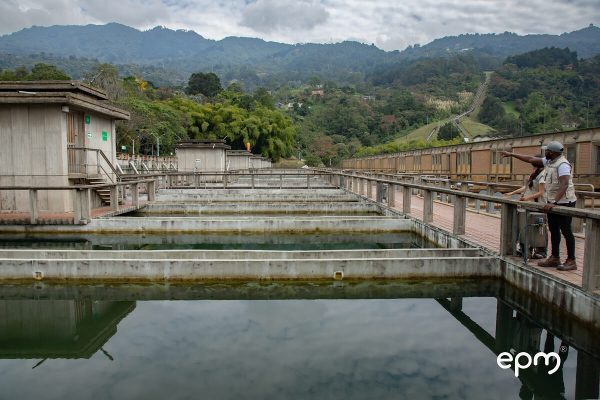 Tanques de agua y estructuras en concreto de la planta La Ayurá, con dos personas observando el entorno montañoso. 