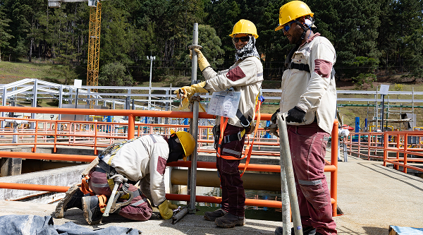 Trabajadores con casco y equipo de seguridad realizando labores de mantenimiento o inspección en una planta industrial al aire libre.