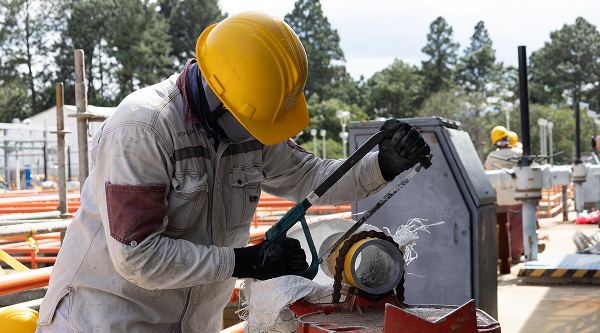 Trabajadores con casco y equipo de seguridad realizando labores de mantenimiento o inspección en una planta industrial al aire libre.