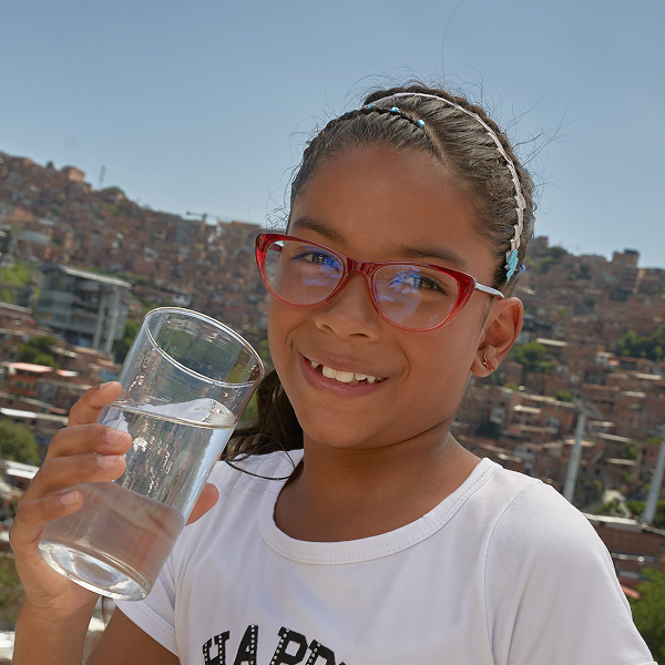 Niña sonriente, con un vaso de agua en su mano derecha