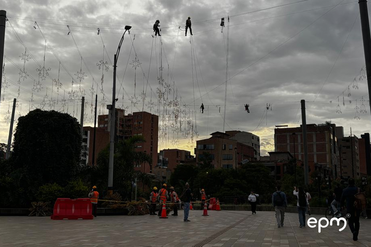 Empleados de EPM colgando figuras navideñas. Al fondo se observan árboles y edificios