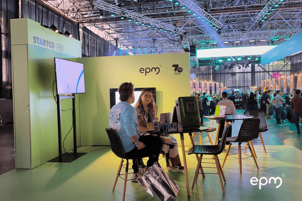 Fotografía de unos representantes de EPM atienden a emprendedores en el stand de Startco 2025, con branding de EPM y el logo de los 70 años en el fondo.