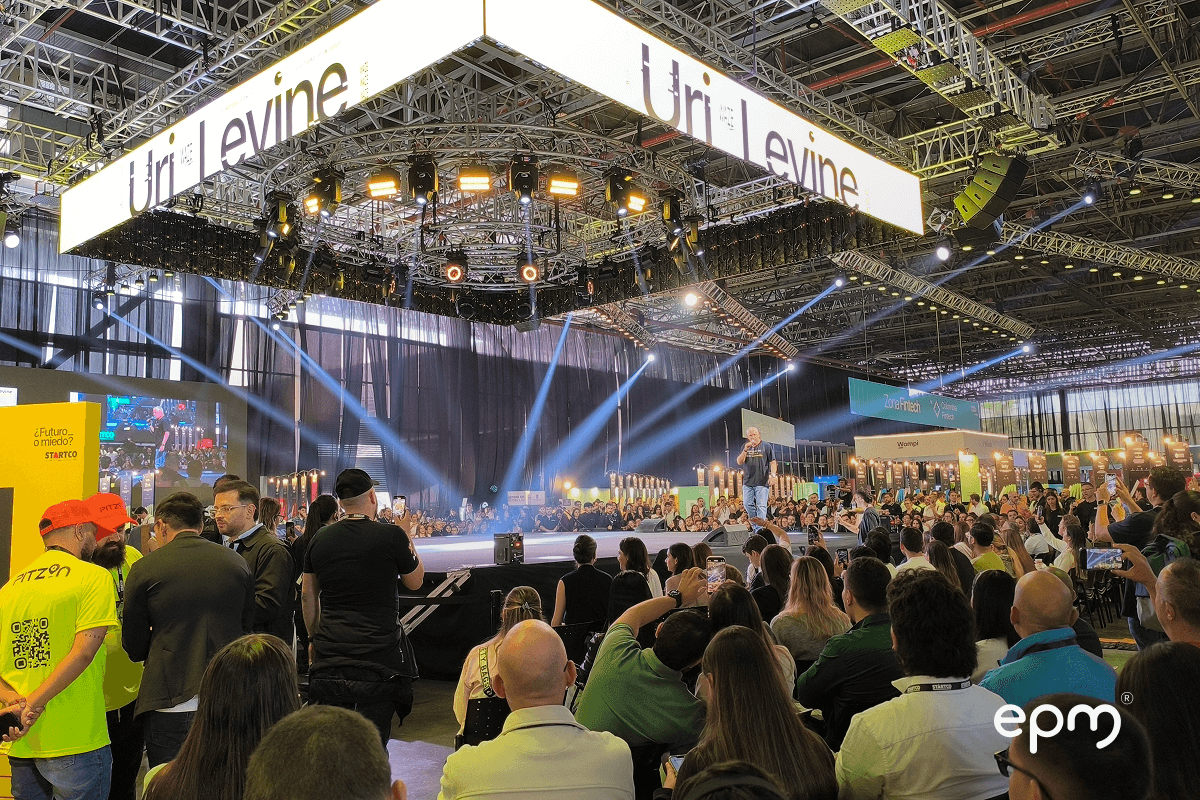 Público asistente al evento Startco 2025 observa la intervención de Uri Levine en el escenario principal bajo una gran estructura de luces y pantallas.