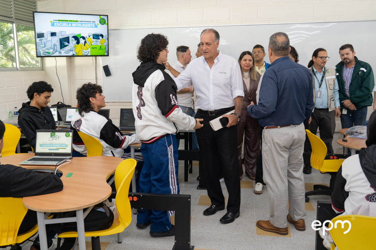 Representantes de EPM conversan con estudiantes en el aula de informática. Al fondo, pantalla con el mensaje "Escuela Inteligente"