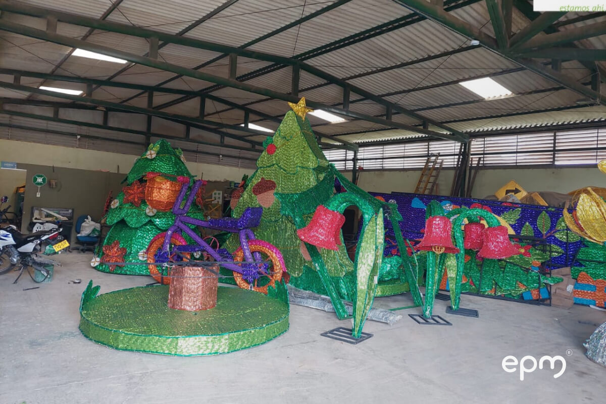 Decoraciones navideñas coloridas con árboles, campanas y bicicleta en un taller, acompañadas del logo de EPM.