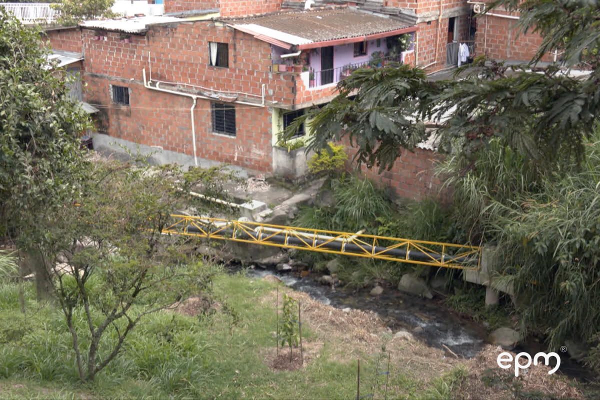 Fotografía de unas viviendas de ladrillo en una zona con vegetación, con una tubería suspendida en el aire encerrada en hierro amarillo