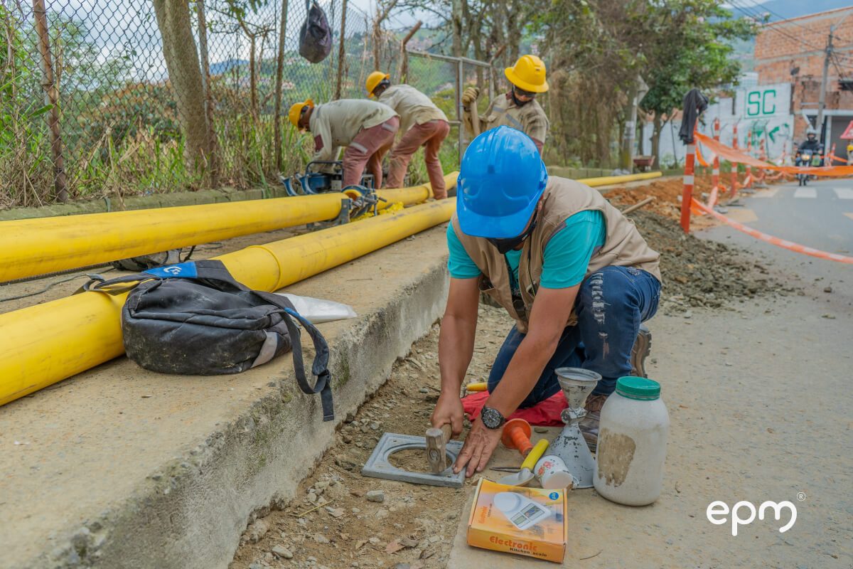 Fotografía de trabajador con casco azul y chaleco de seguridad realiza una conexión de gas en la vía