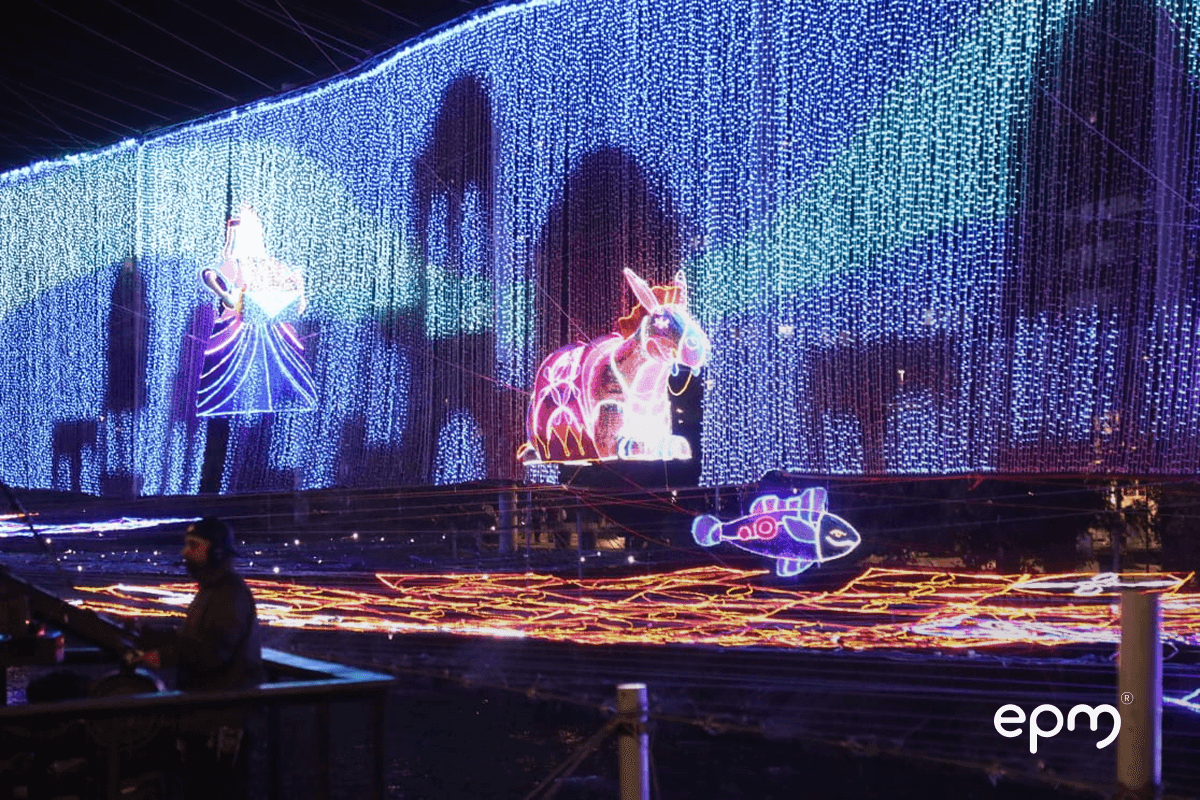 Fotografía de una escena nocturna de los alumbrados navideños de EPM con figuras luminosas de ángeles, animales y peces sobre un río iluminado.