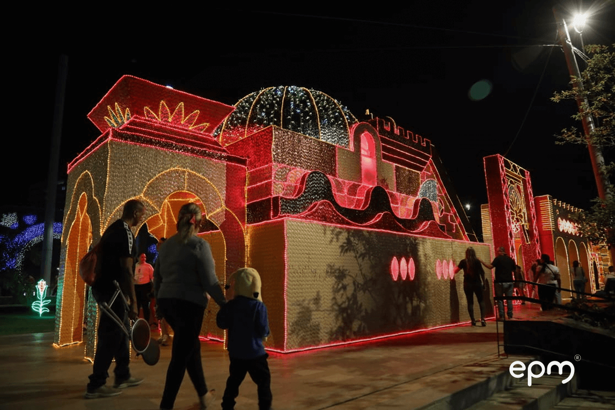 Fotografía de familias que recorren una estructura luminosa navideña con forma de castillo iluminado en tonos rojos, amarillos y rosados.