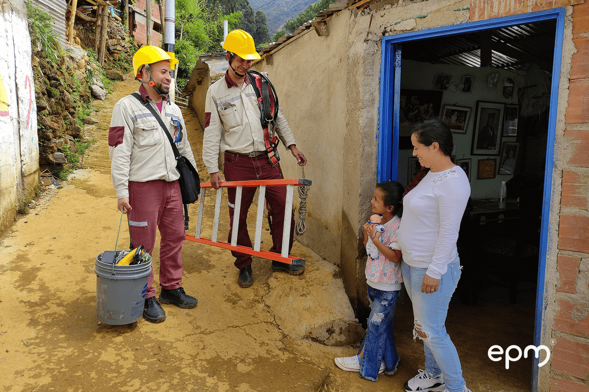 Fotografía de técnicos de EPM visitan una vivienda rural, conversando con una madre y su hija en la puerta de su hogar, como parte de un proyecto comunitario.