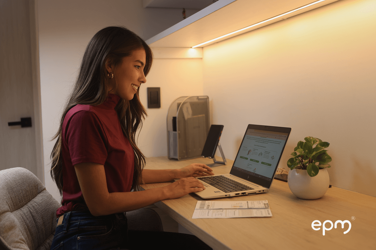 Fotografía de mujer joven revisa su factura de servicios públicos en el portal de EPM desde su computador portátil en casa.