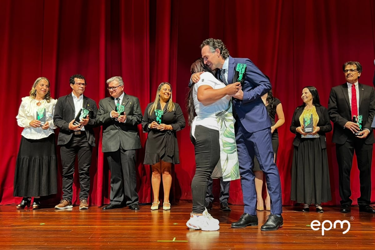 Momento emotivo en la ceremonia de los 70 años de EPM, donde un homenajeado recibe reconocimiento en el escenario acompañado de diferentes invitados