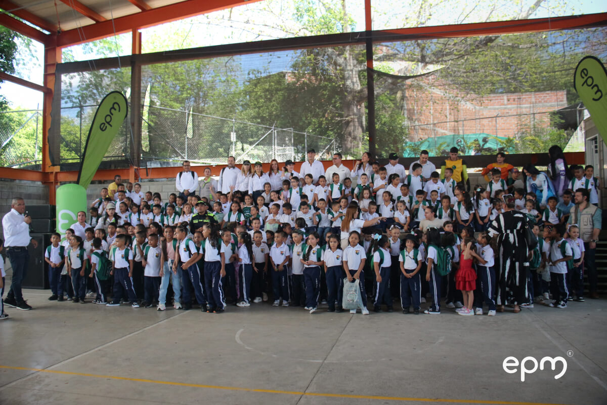 Niños sonrientes recibiendo paquetes escolares de EPM en un acto educativo.