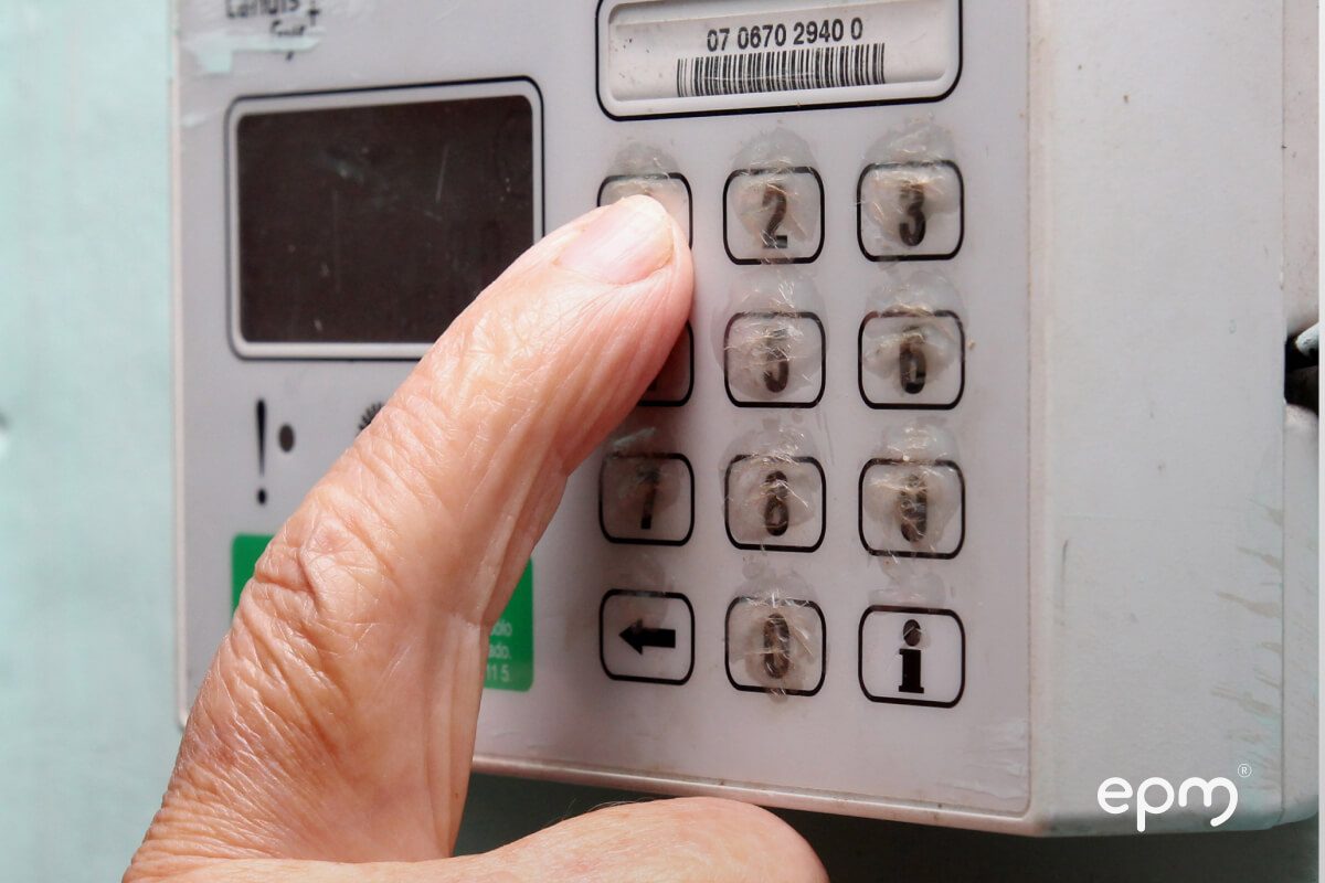 Fotografía de primer plano de una mano introduciendo un código en un medidor de energía prepago.