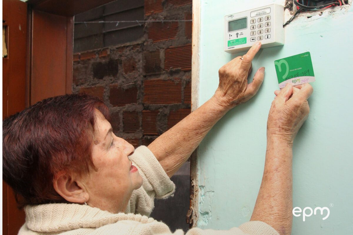 Fotografía de un mujer mayor utiliza una tarjeta prepago para activar un medidor de energía en su hogar.
