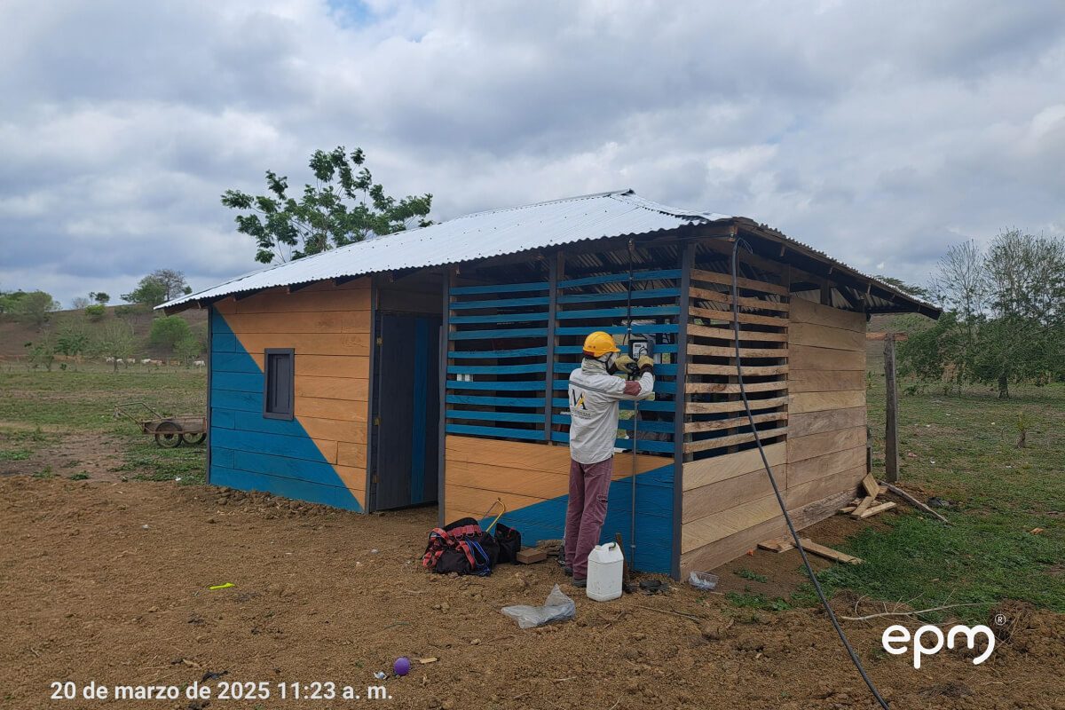 Fotografía de un técnico con casco amarillo y uniforme trabaja en la instalación de energía en una vivienda rural de madera.