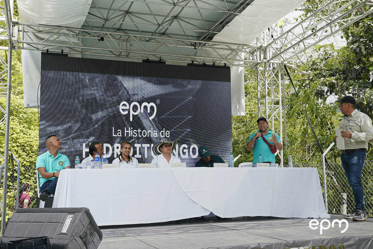 Personas sentadas alrededor de una mesa. De fondo se observa pantalla con el logo de EPM