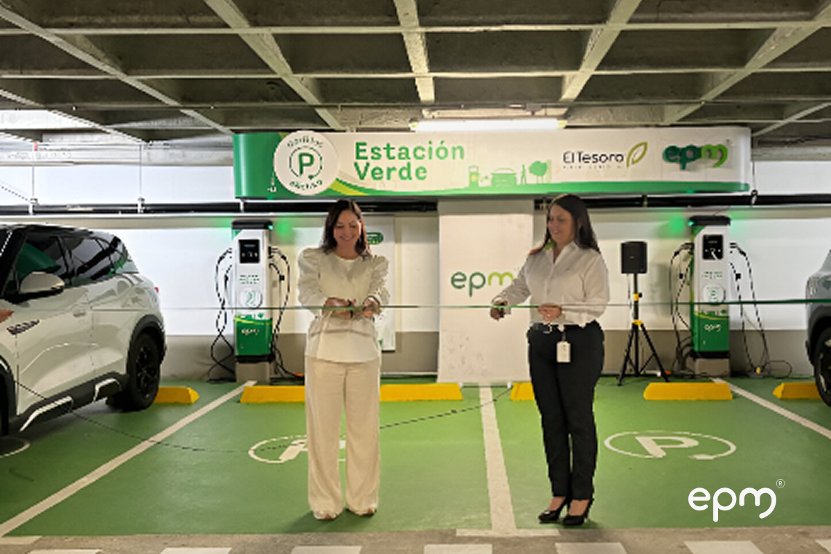 Fotografía de dos mujeres cortan una cinta en la inauguración de una "Estación Verde" de carga para vehículos eléctricos en un estacionamiento.