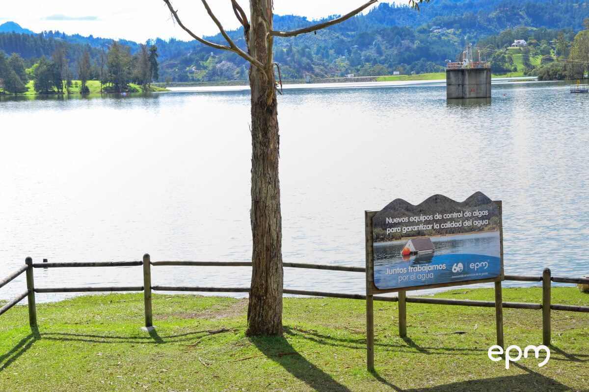 Fotografía de un embalse con un cartel informativo sobre nuevos equipos de control de algas implementados por EPM para asegurar la calidad del agua.