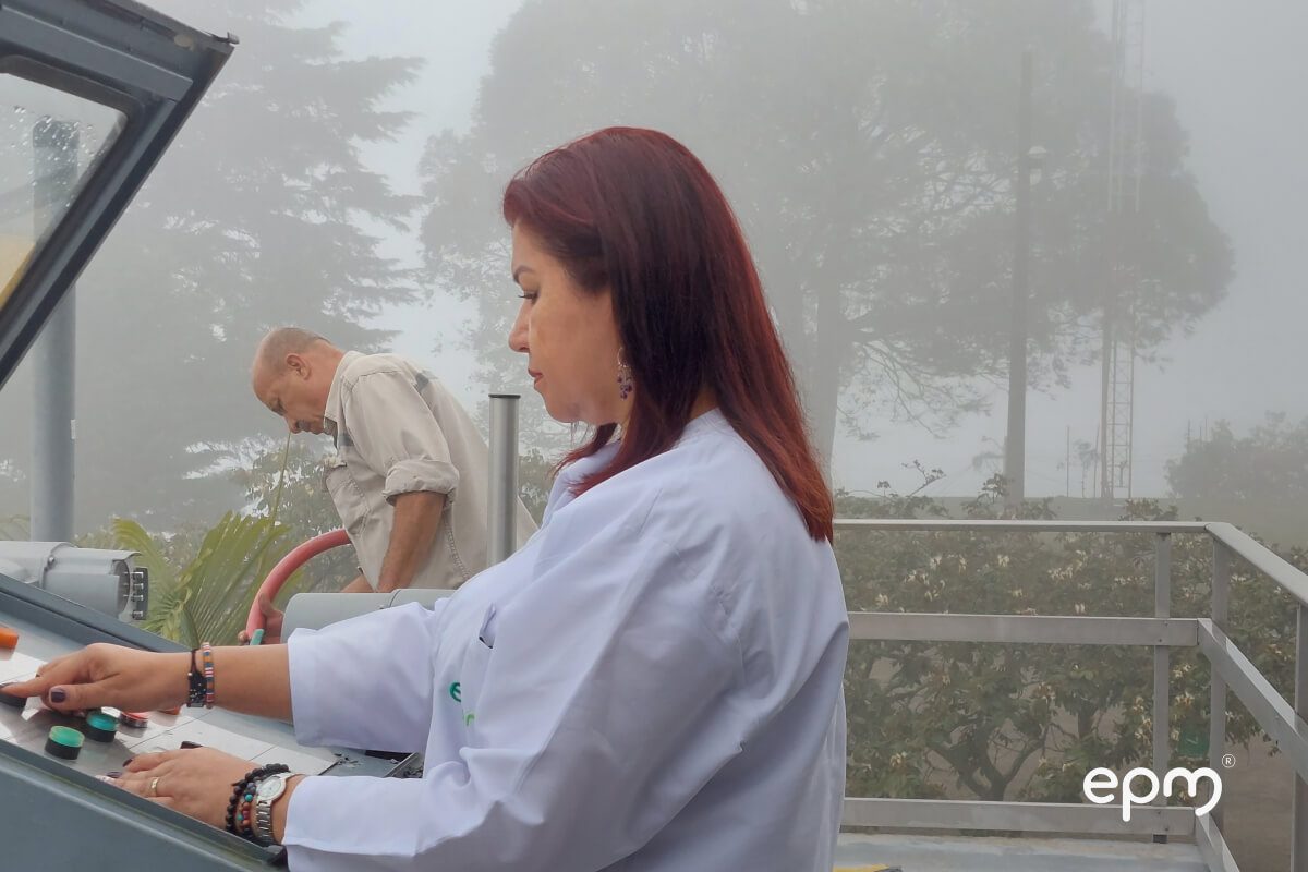 Fotografía de científica de EPM en laboratorio al aire libre, operando maquinaria de monitoreo de calidad del agua en una zona montañosa con neblina.