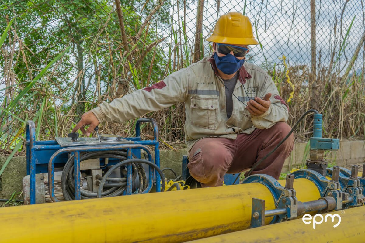 Fotografía de operario con casco y mascarilla supervisando la instalación de tuberías de gas natural en una zona al aire libre con vegetación.