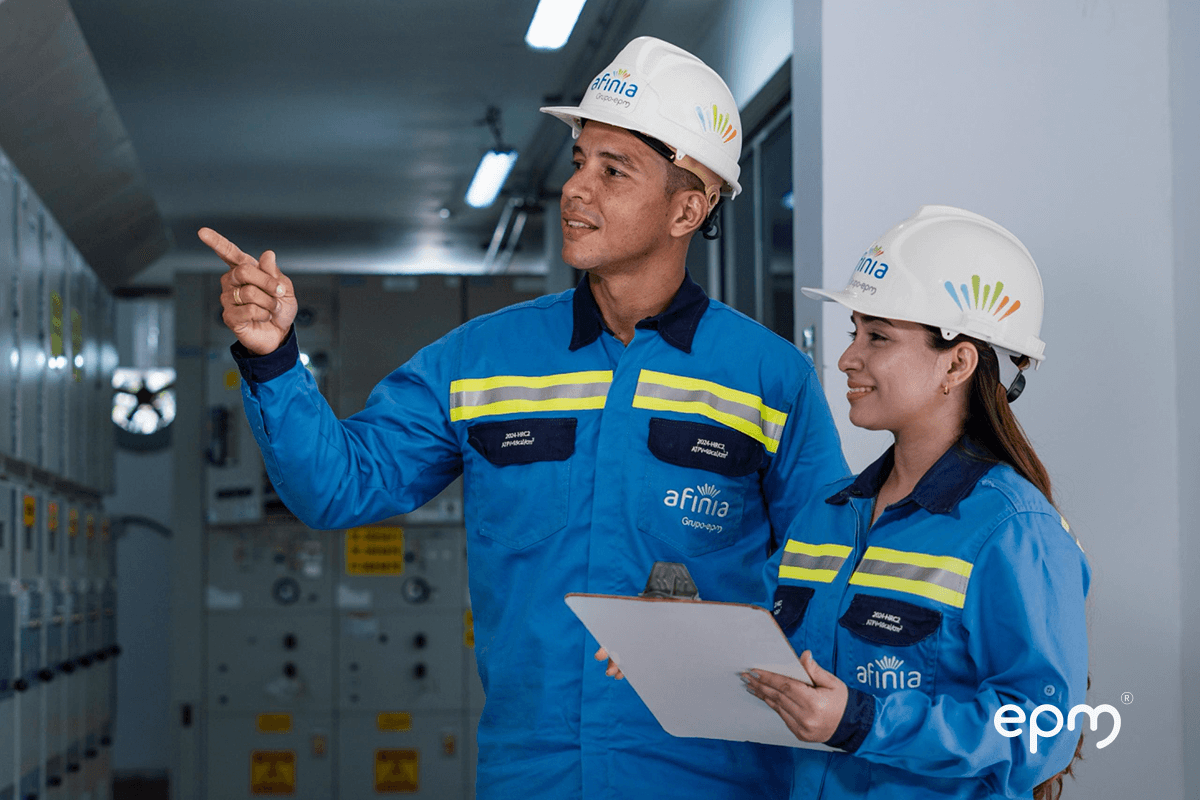Fotografía de dos trabajadores de Afinia, con casco y uniforme, inspeccionan equipos eléctricos en una subestación.