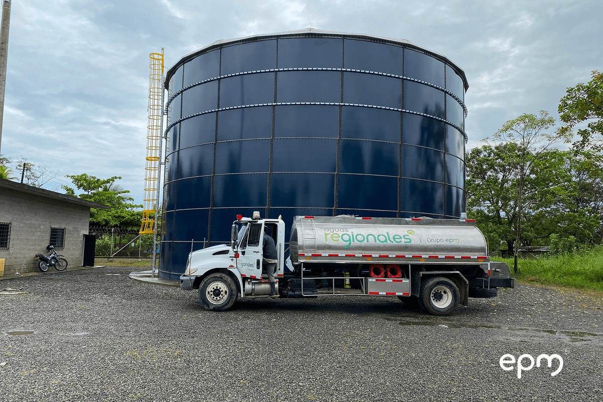 Fotografía de un camión transportador de agua frente a un tanque grande que la almacena 