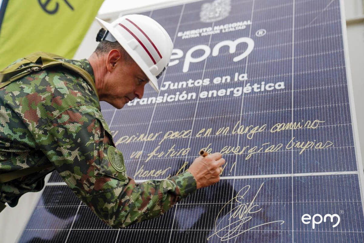 Fotografía de militar del Ejército Nacional de Colombia firma un gran panel solar con el logo de EPM y la frase "Juntos en la transición energética"