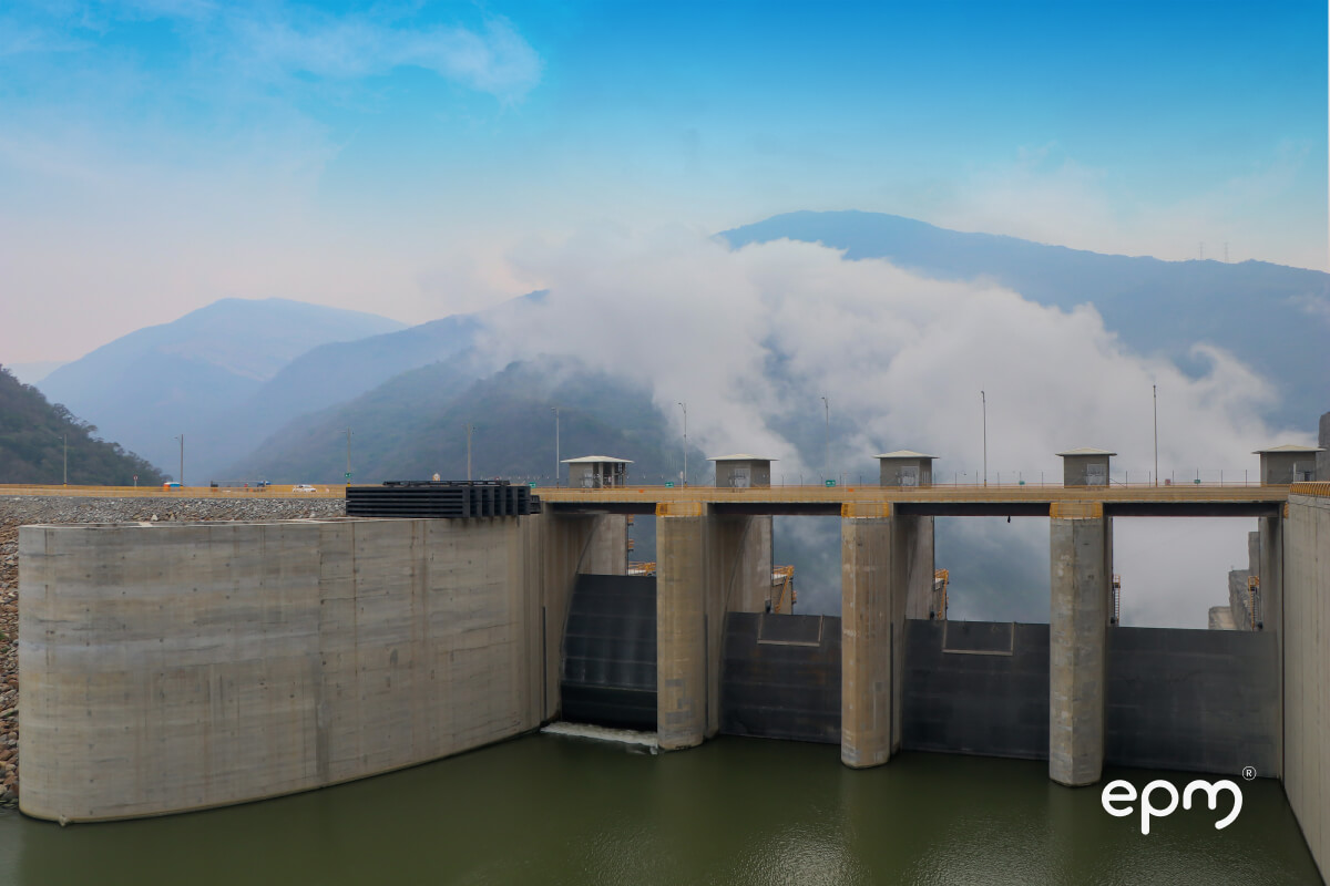 Estructura de la presa de Hidroituango con compuertas y embalse, rodeada de montañas.