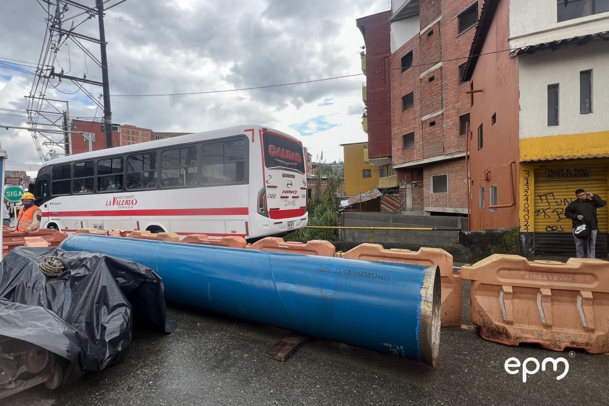 Fotografía de una obra en vía urbana con un gran tubo azul colocado en el suelo, delimitado por barreras de seguridad anaranjadas.