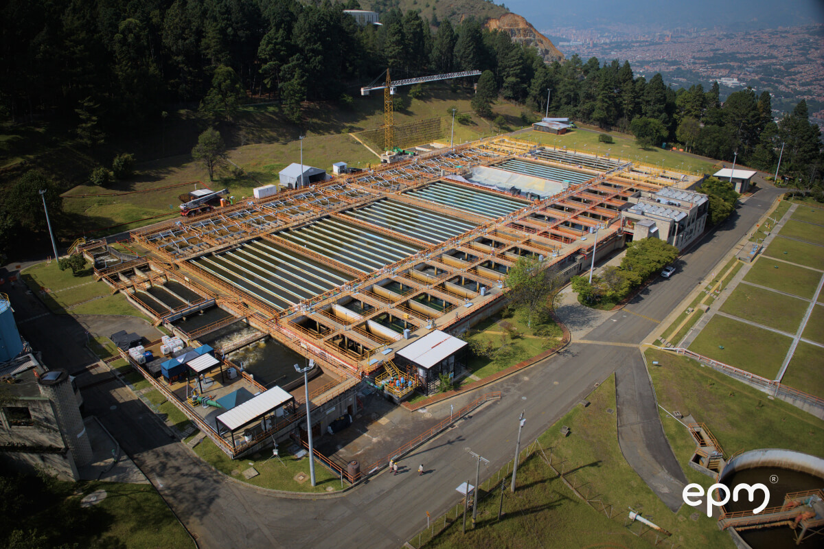 Imagen de la vista aérea de una gran planta de tratamiento de agua con múltiples tanques y estructuras, rodeada de vegetación.