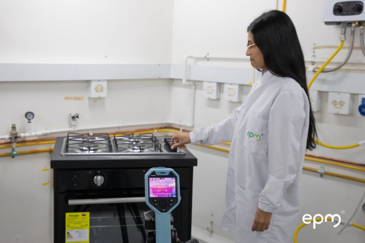 Fotografía de técnica de laboratorio de EPM encendiendo una estufa de gas mientras un dispositivo térmico mide la temperatura.