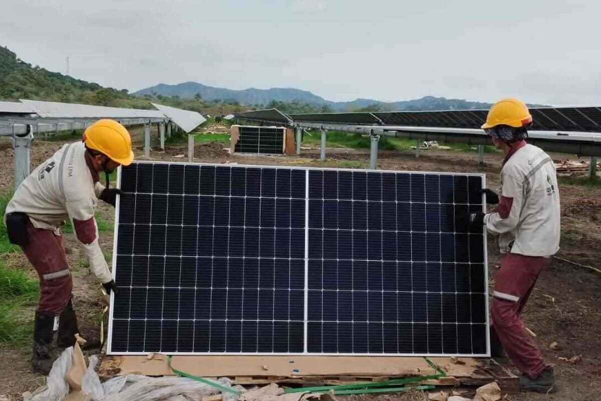 Fotografía de dos trabajadores con cascos amarillos levantan y colocan un panel solar en su estructura
