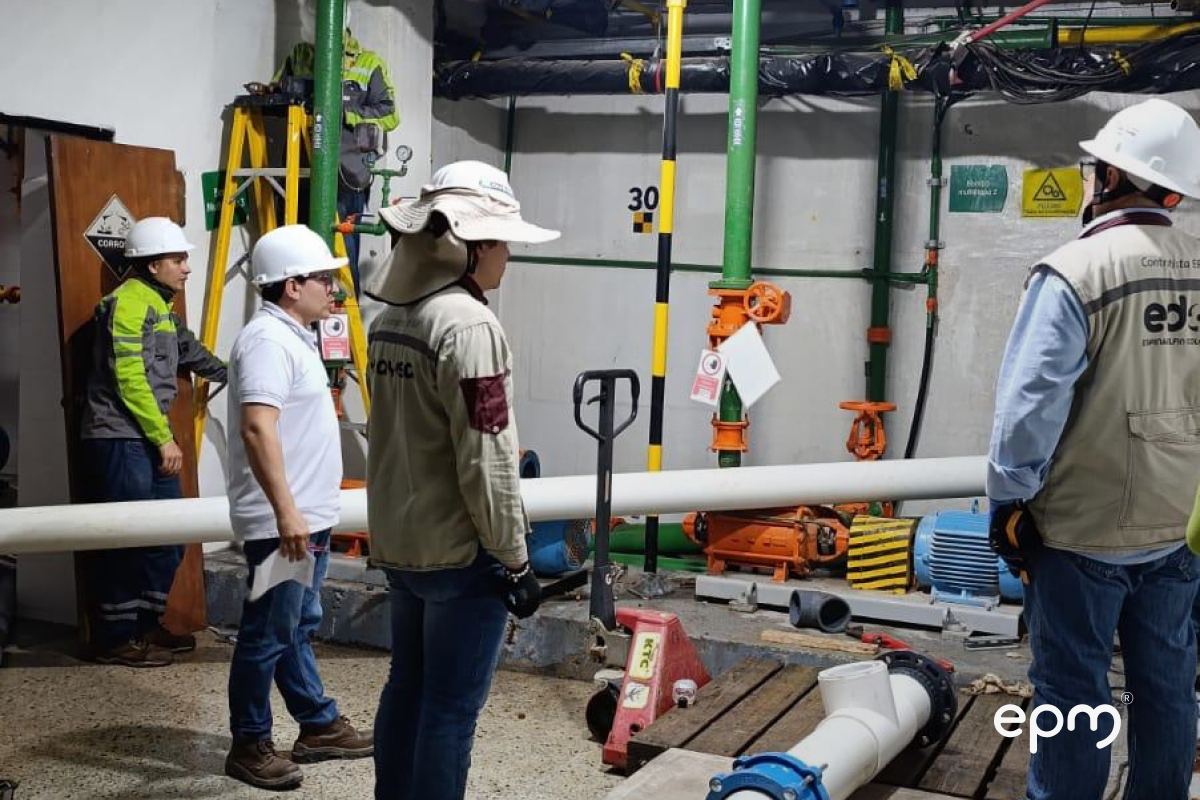 Trabajadores de EPM con cascos de seguridad supervisan tuberías y equipos en una sala técnica subterránea
