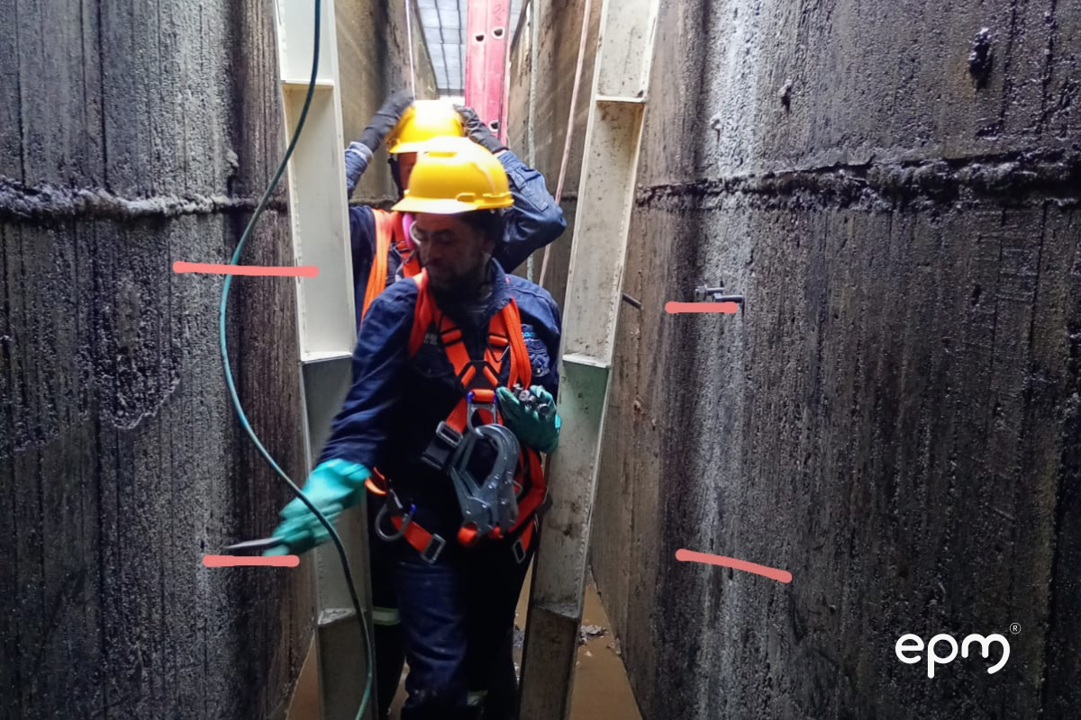 Operarios con arnés y casco de seguridad realizan labores dentro de un canal estrecho de concreto.