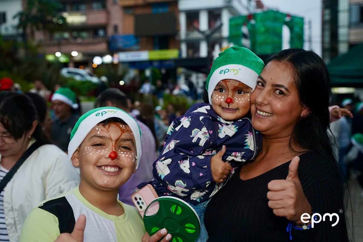 Mujer y dos niños sonriendo. Tiene la cara pintada y usan gorros de navidad