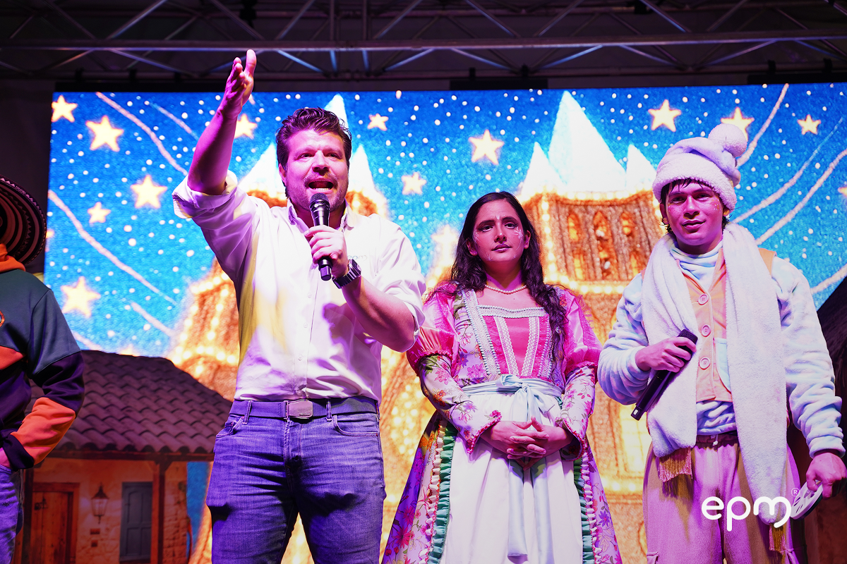 Actores de obra de teatro en escenaro con micrófono en mano. De fondo se observa pantalla con imágenes alusivas a la navidad