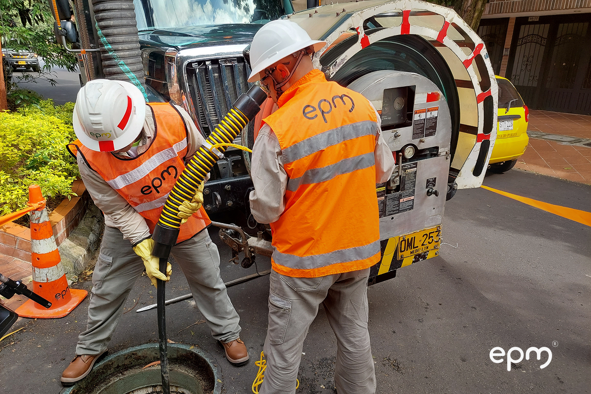 Funcionarios de EPM con casco blanco y uniforme naranja realizando labores de mantenimiento en alcantarillado de Medellín