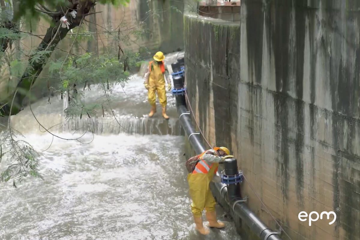 Fotografía de personal de EPM con trajes de seguridad inspeccionando y trabajando en un canal de aguas lluvias con tuberías expuestas.