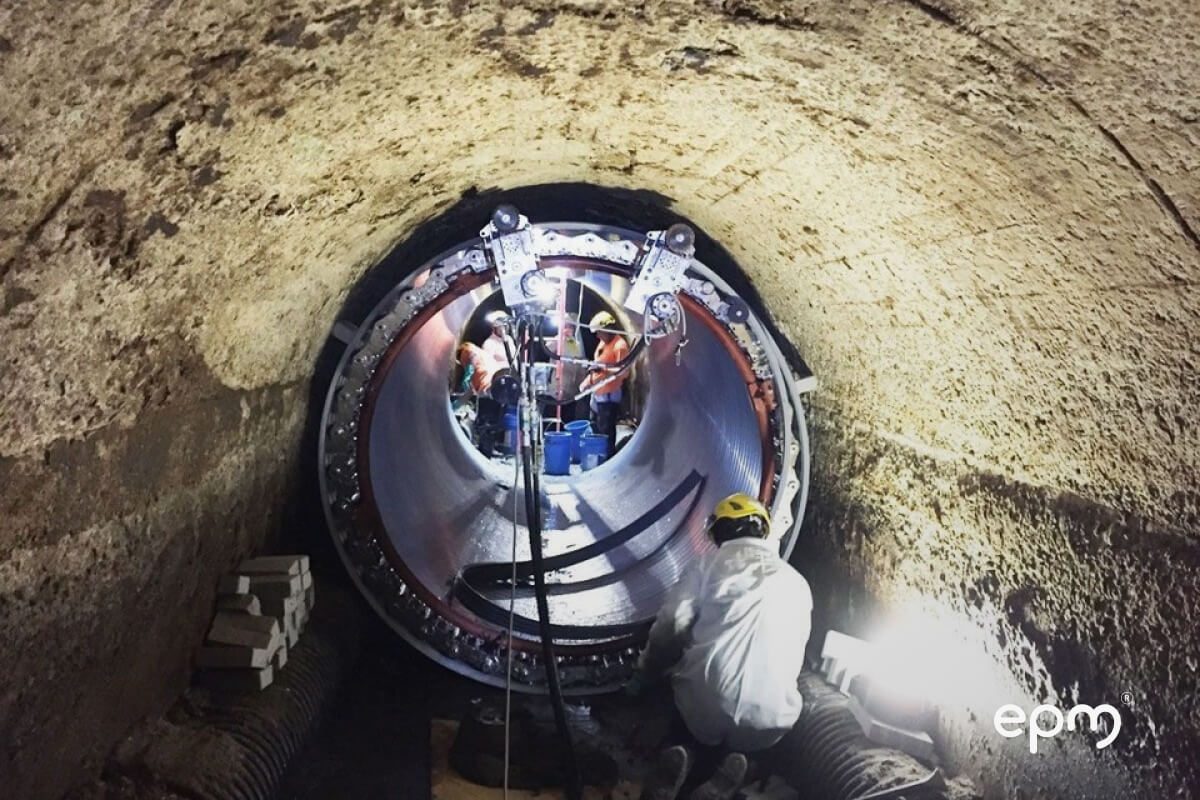 Fotografía de equipo de trabajadores de EPM dentro de un túnel subterráneo realizando mantenimiento en una gran tubería.