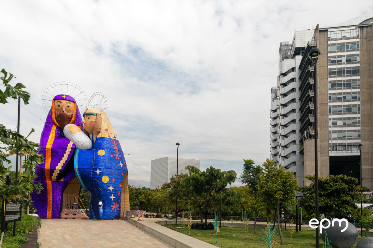 Escultura iluminada del pesebre navideño con figuras de José, María y el niño Jesús, ubicadas en un parque junto a la sede principal de EPM en Medellín.
