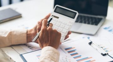 Persona trabajando en una computadora portátil y revisando documentos, representando instrumentos económicos y gestión financiera.