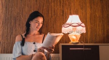 Mujer leyendo un libro en una sala de estar, simbolizando el acceso a servicios públicos y la comodidad del hogar.