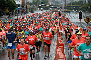una multitud de personas con camisetas rojas participando en una carrera atlética sobre una avenida cerrada al tráfico.