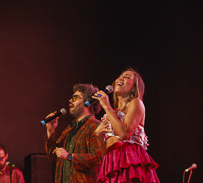 Dúo de cantantes actuando en vivo con gran energía bajo luces de escenario.