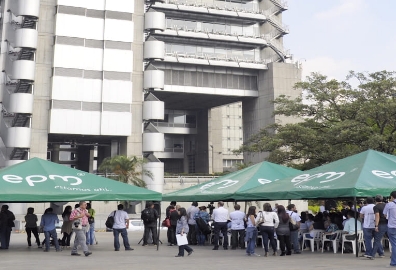 Personas reunidas bajo carpas verdes de EPM frente al edificio principal de la empresa en Medellín
