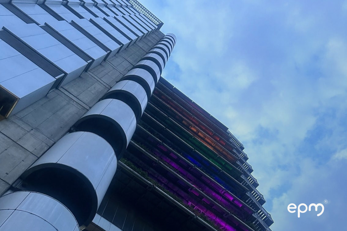Vista en contrapicado de un edificio moderno con fachada arquitectónica y elementos verticales, iluminado con colores, bajo un cielo azul