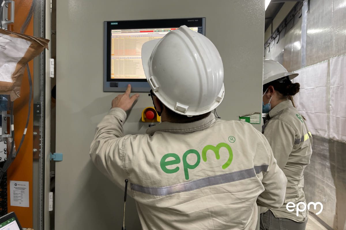Dos técnicos de EPM con cascos de seguridad operando una pantalla de control industrial
